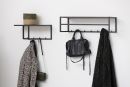 Moderne Garderobe mit Haken, schwarzer Tasche, Mantel, Schal und Korb an weißer Wand im Flur.