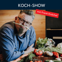 Koch Frank Knöchel in Koch-Show, umgeben von frischem Gemüse, hält Lauch humorvoll unter der Nase.