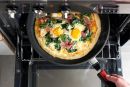 Pizza mit Spinat, Schinken und zwei Eiern wird in einer Pfanne im Backofen gebacken, Draufsicht.