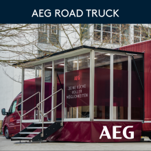 AEG Road Truck mit gläsernem Showroom, rotem Branding und Slogan „Deine Küche voller Möglichkeiten“ vor Gebäuden.