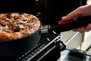 Frischer Kuchen in beschichteter Pfanne wird mit abnehmbarem Griff aus dem Backofen genommen.