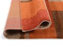 Moderner Teppich in Orange- und Brauntönen, gefaltet, weiche Oberfläche, geometrisches Muster, Nahaufnahme.