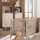 Modernes Babyzimmer mit Holz-Babybett, Kuschelteddy, Schrank und Tageslicht, gemütlich und kinderfreundlich eingerichtet.