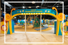 Bunter Eingang zum Kinderspielbereich „Circus Francesco Rieger“ mit Klettergerüst und Zirkusdeko im Innenraum.  