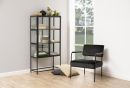 Modernes Wohnzimmer mit schwarzem Sessel, Glastür-Vitrine, Pflanzen, Büchern und Kissen auf hellem Holzboden.
