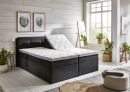 Modernes Boxspringbett mit grauem Stoffbezug, hohem Kopfteil und weißer Matratze, freigestellt auf weißem Hintergrund.