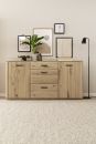 Sideboard aus Eiche mit Dekoration, Zimmerpflanze, Bilderrahmen und Stehlampe in modernem Wohnzimmer.