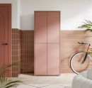 Moderner, rosafarbener Schrank vor gefliester Wand im Flur mit Fahrrad und Zimmerpflanzen, minimalistisches Design.