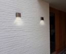Moderne Außenwandleuchten an weißer Klinkerwand neben Holztür, energiesparende LED-Beleuchtung für Hausfassade.
