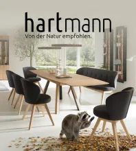 Werbebanner der Marke Hartmann mit dem Slogan „Von der Natur empfohlen“. Gezeigt wird ein moderner Essbereich mit Holztisch und schwarzen Stühlen, am Boden sitzt ein Dachs zwischen herbstlichem Laub.