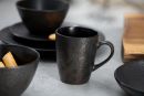 Schwarzes, strukturiertes Keramikgeschirr mit Tasse, Schalen und Tellern auf grauem Tisch, modernes Design.