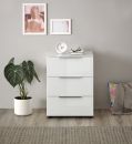 Weiße Kommode mit drei Schubladen, Zimmerpflanze, Uhr, Brille und Wandbildern in modernem Wohnzimmer.