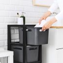 Person stellt Handtuch in schwarzen Aufbewahrungskorb im modernen Badezimmer mit weißer Fliesenwand ab.